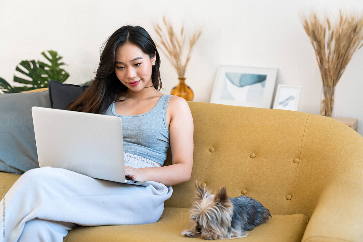 Woman using a laptop while sitting on the sofa with her dog.
