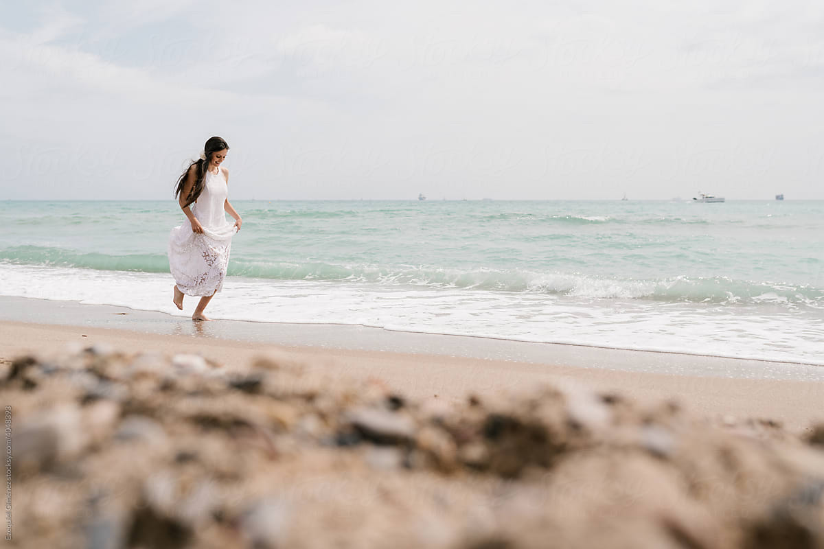 Young bride in white dress running on the beach