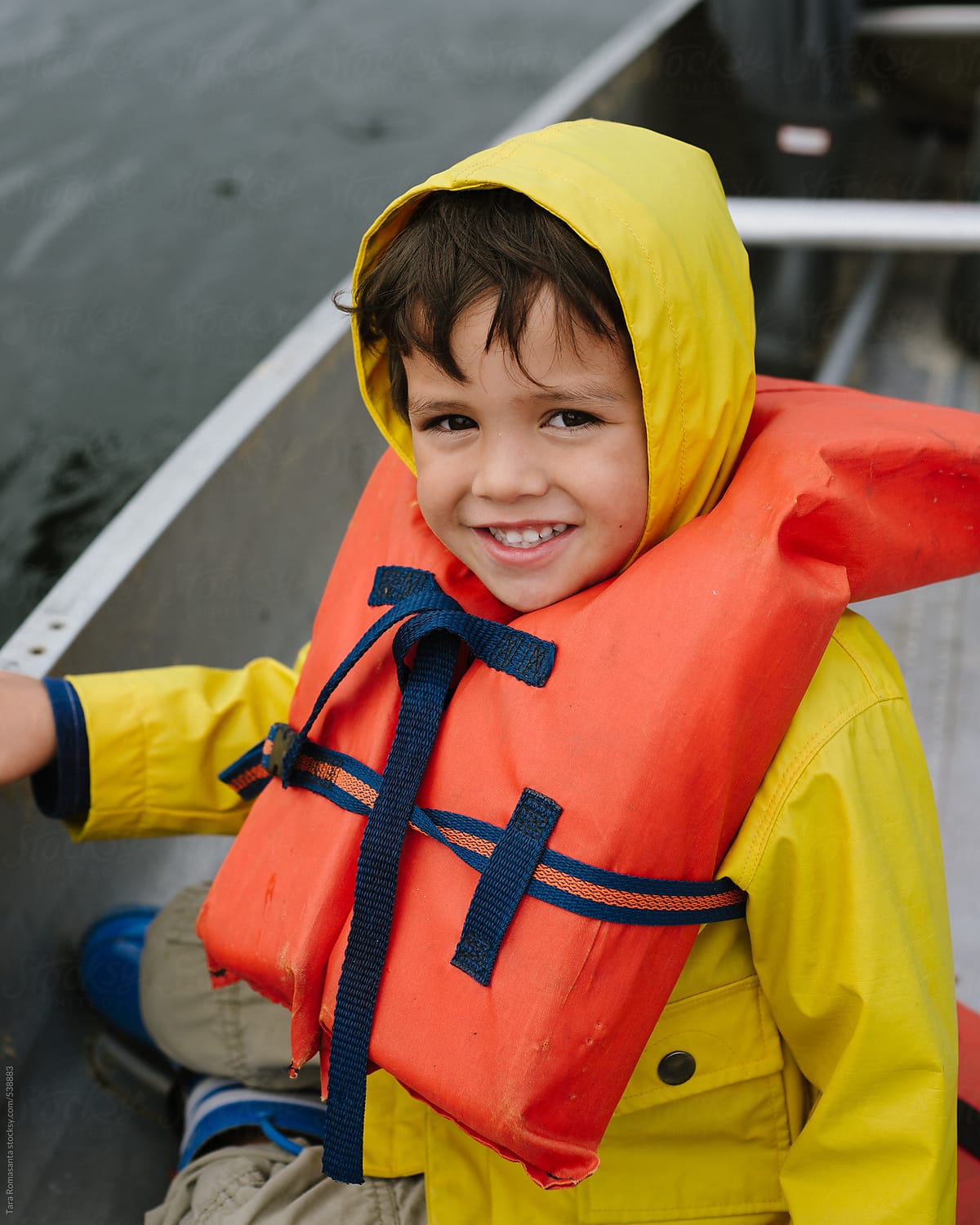 little boy in a rain jacket and life jacket in a canoe