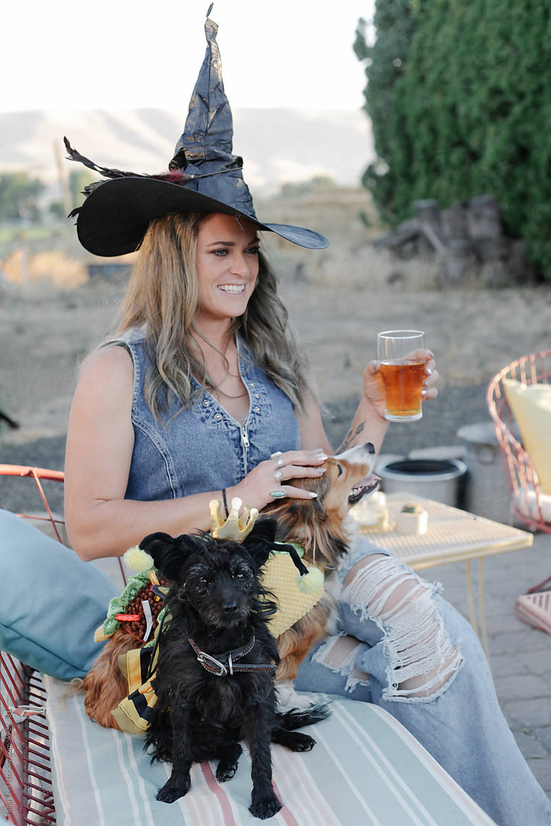 woman in witch hat sits with  dog in costume enjoying the evening