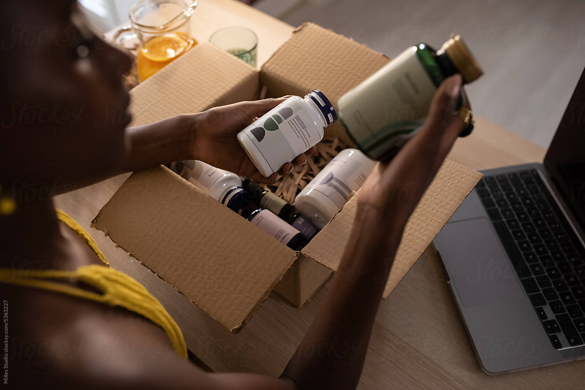 Crop black woman opening box with vitamins on table