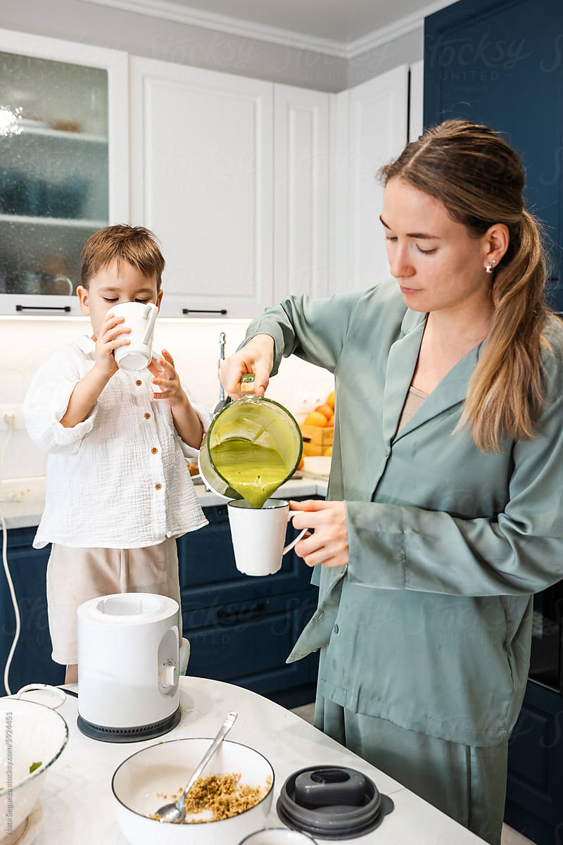 A woman pours a smoothie and her son drinks the beverage