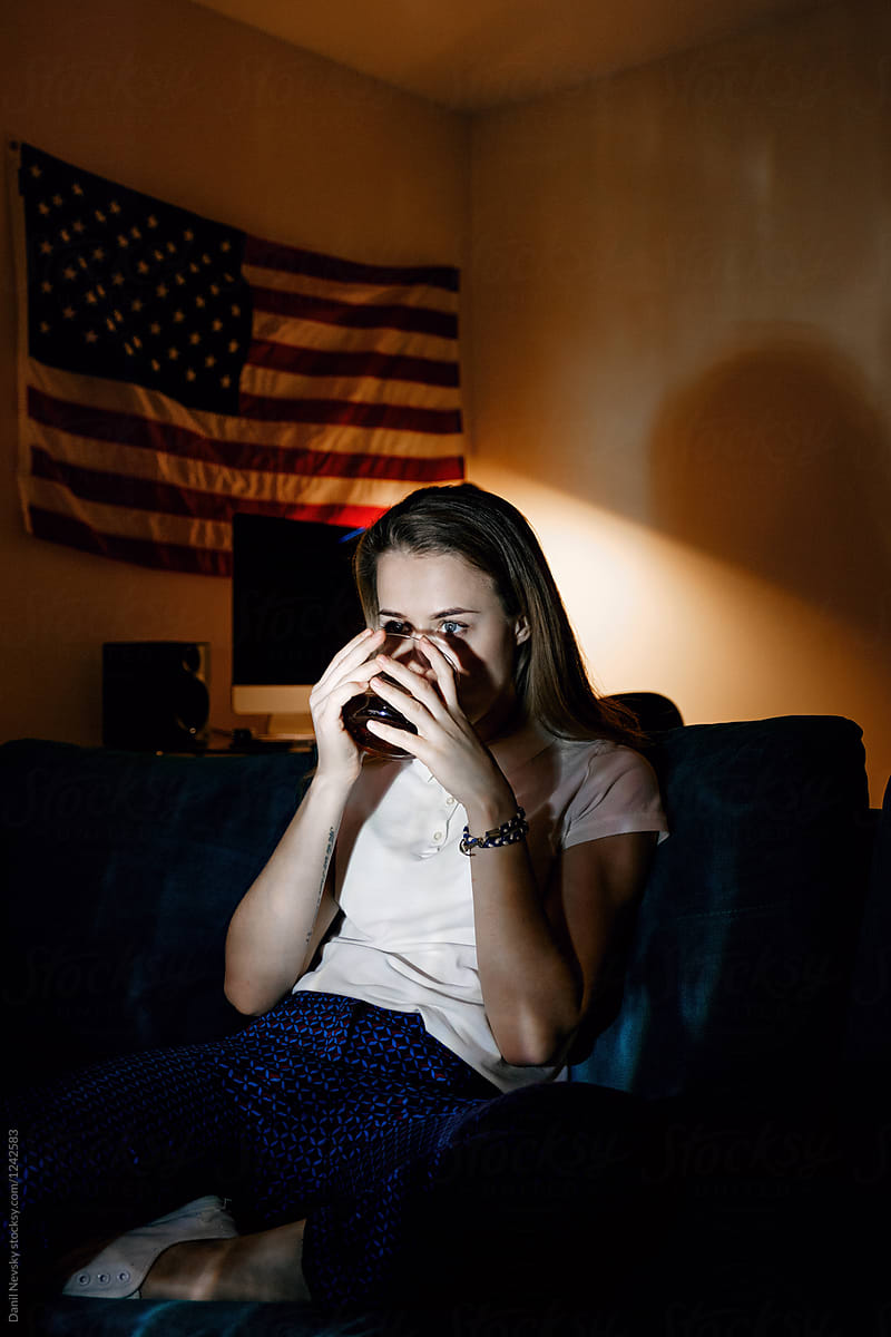 Girl drinking coffee in darkness watching tv. Fourth of July