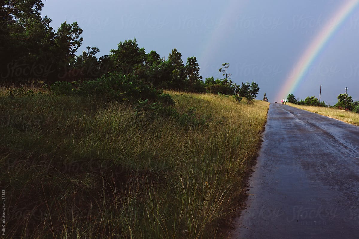 Double rainbow with three men walking on paved road