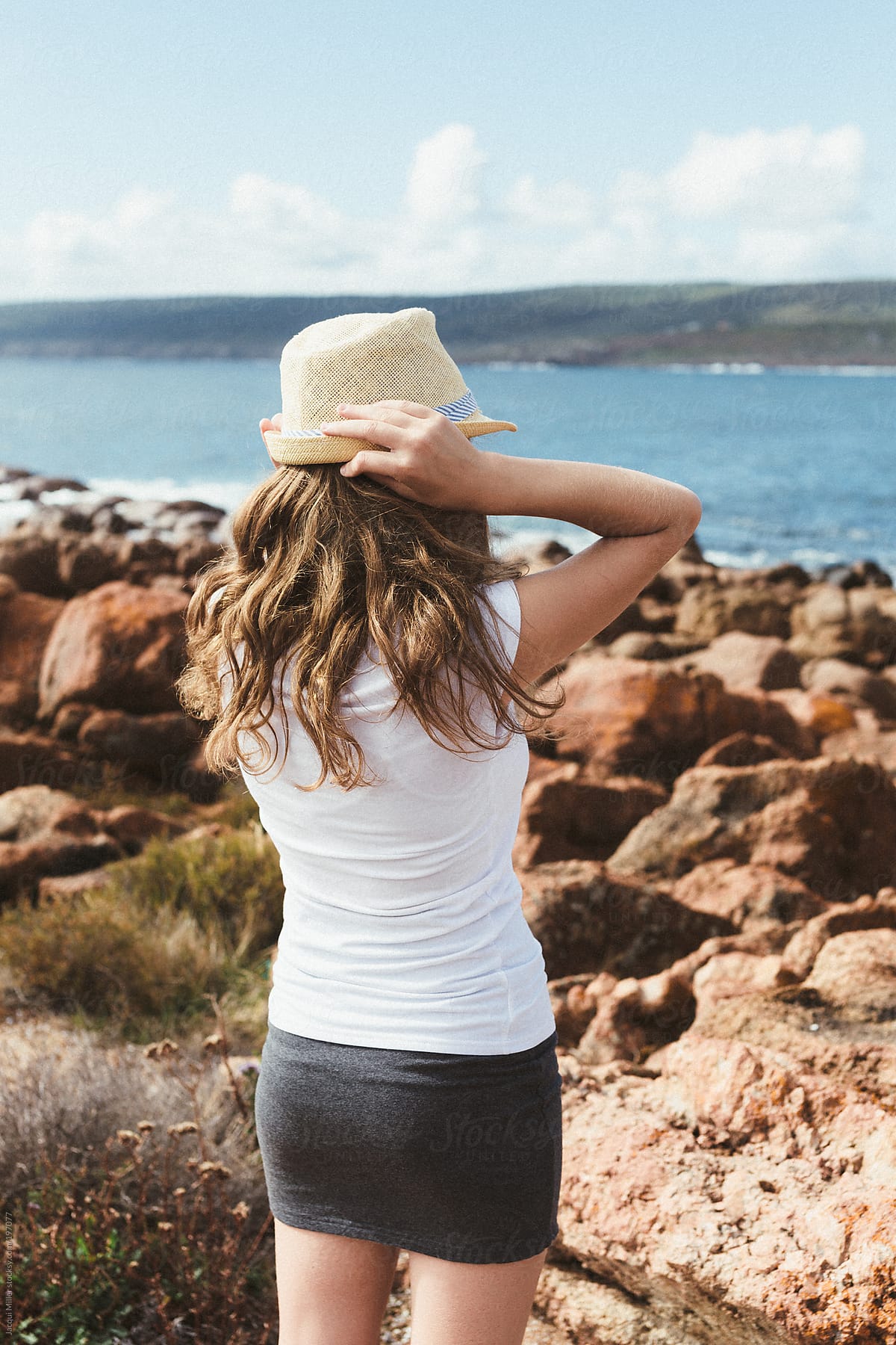 Back View Of Cute Teenage Girl Holding Her Hat On Her Head While Looking Out At The Ocean By 9445