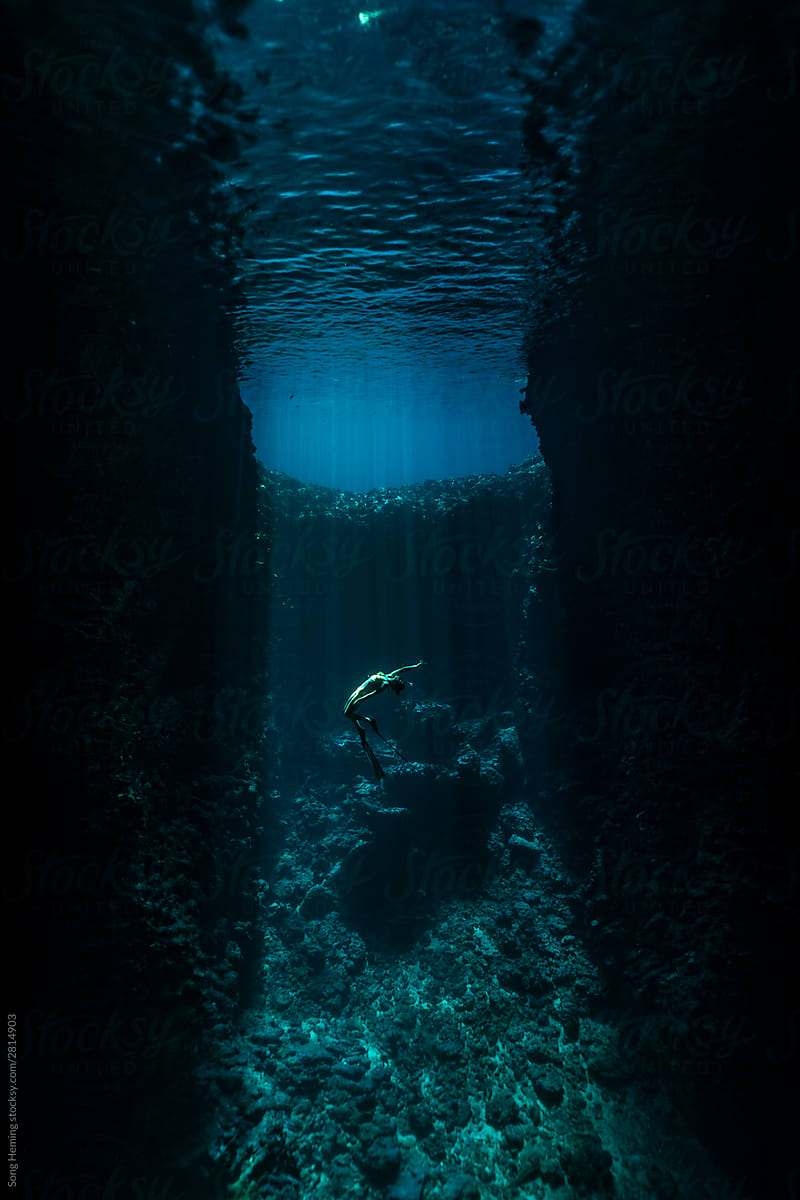 A female freediver with bikini and fins diving in the cave with sun rays