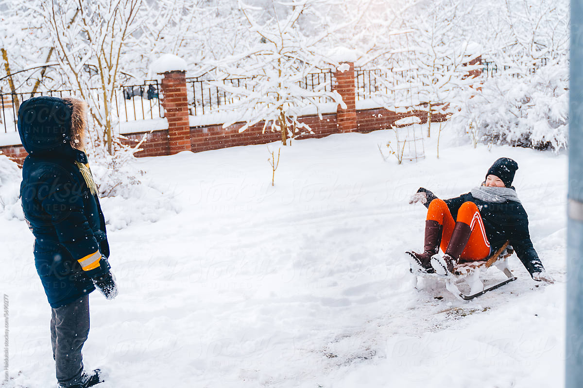 Kids riding sleds in snowy backyard, enjoying holiday season in winter