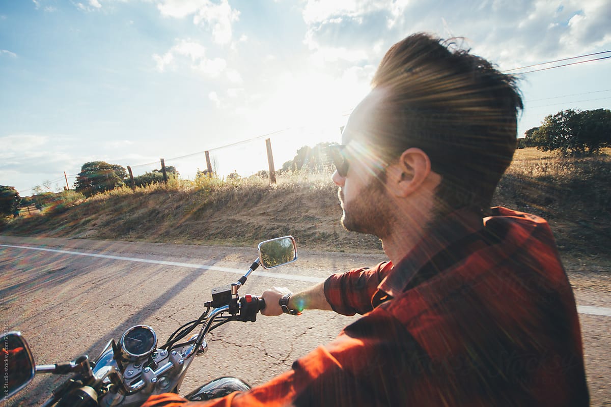 Man in shirt with sunglasses driving his motorbike on a road at sunset