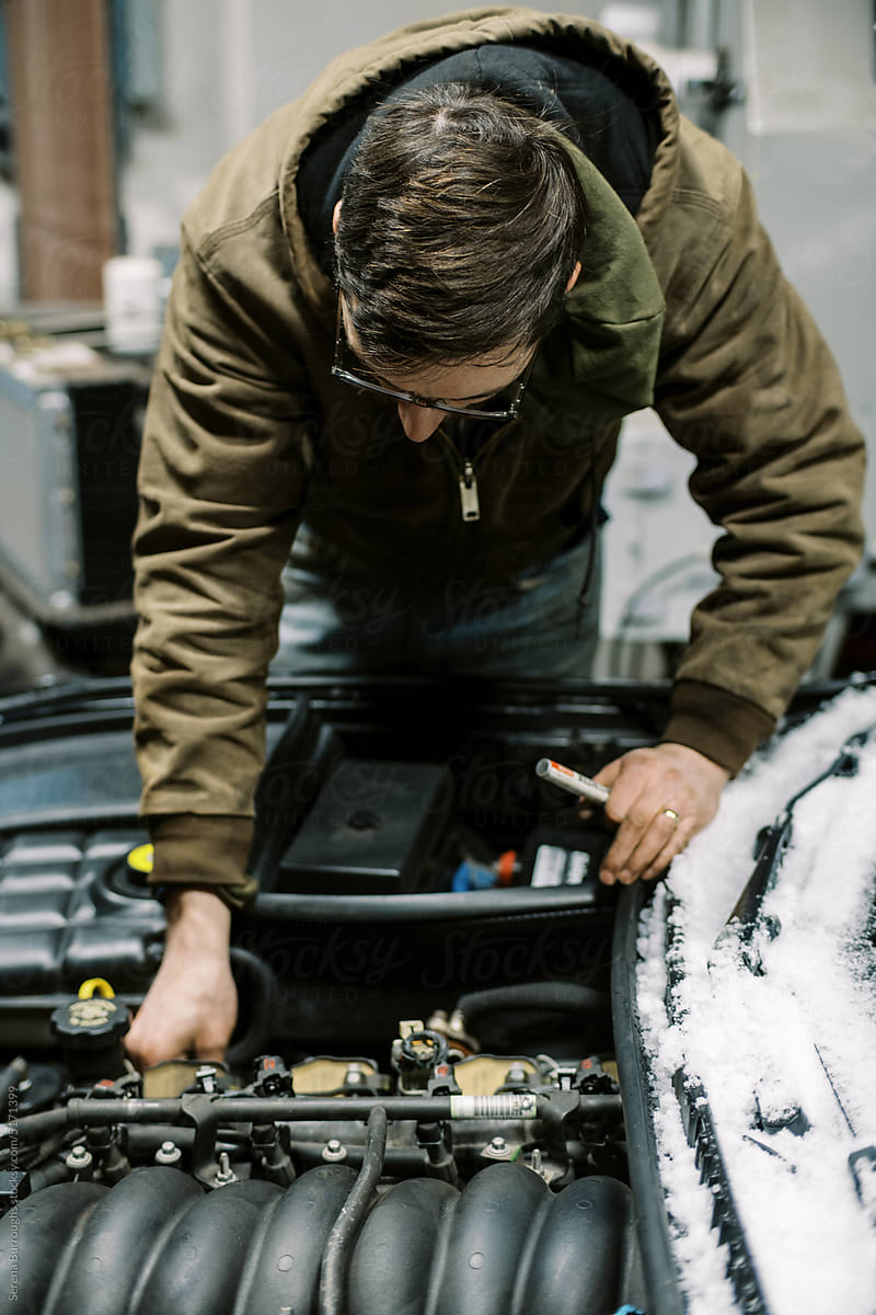 Mechanic wearing winter coat working on a big car engine in garage