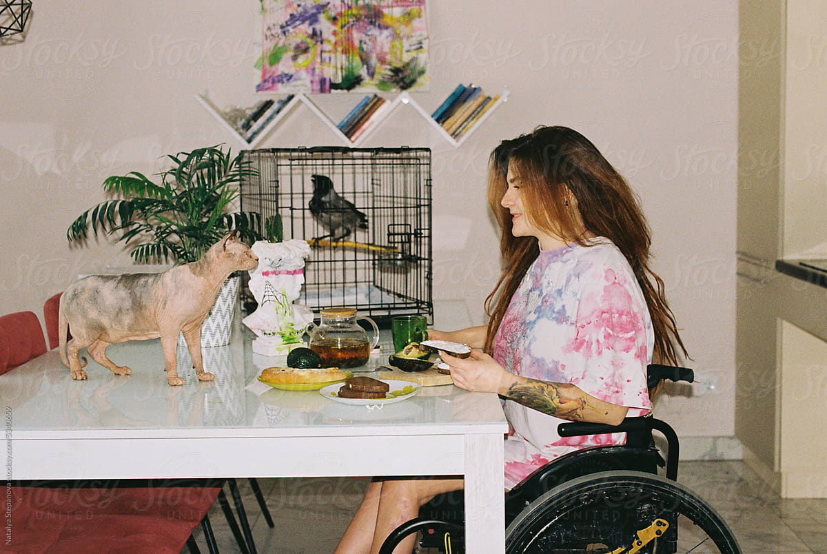 A woman in a wheelchair having breakfast with a cat