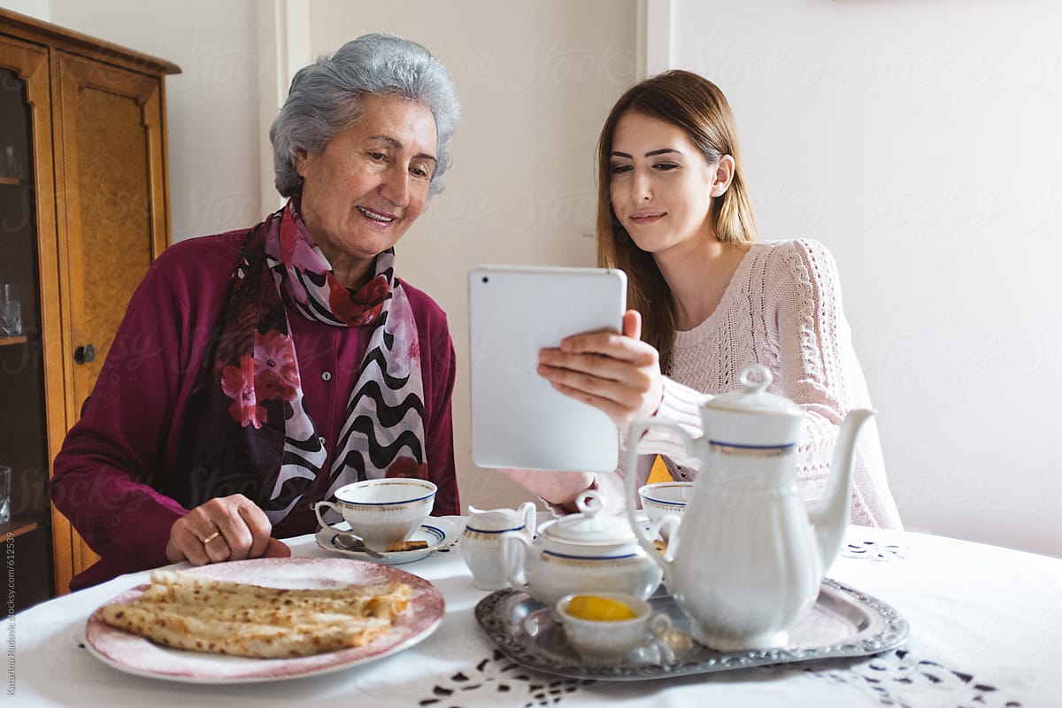 Grandma and Granddaughter Using Tablet Computer while Having a Tea Time
