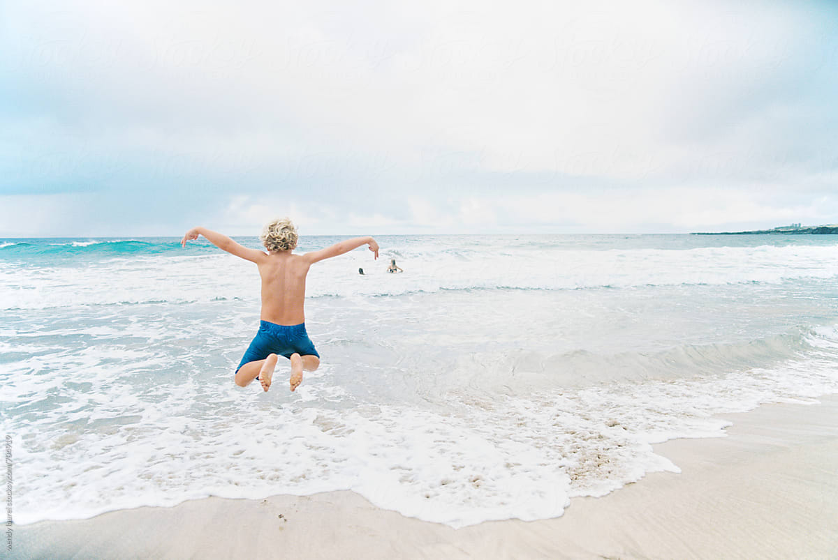little boy jumping for joy at ocean with sunshine and sand