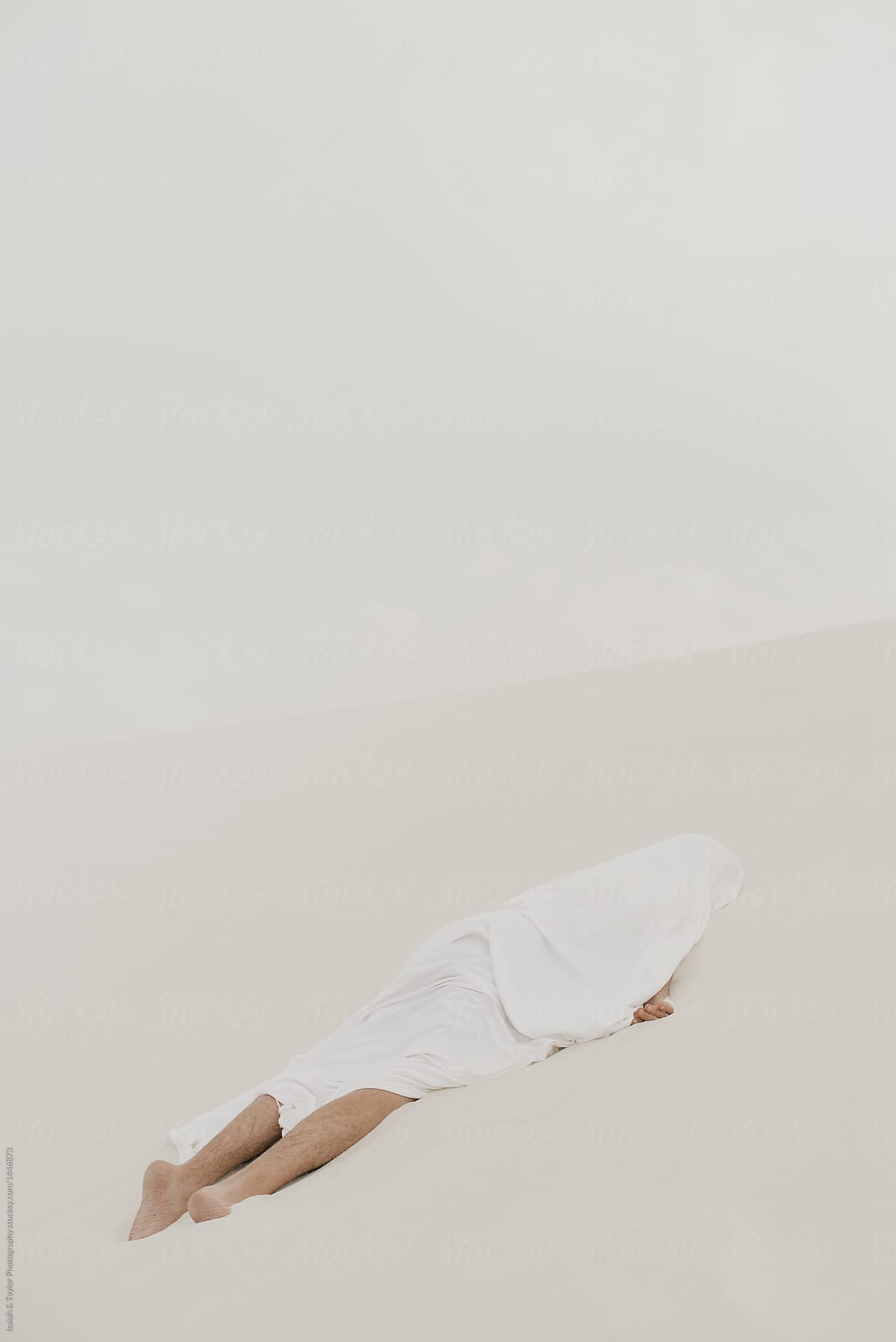 Human laying face down in the sand, white on white minimal concept