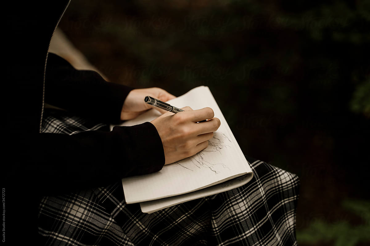 close up of Young woman sitting drawing in notebook in forest during autumn