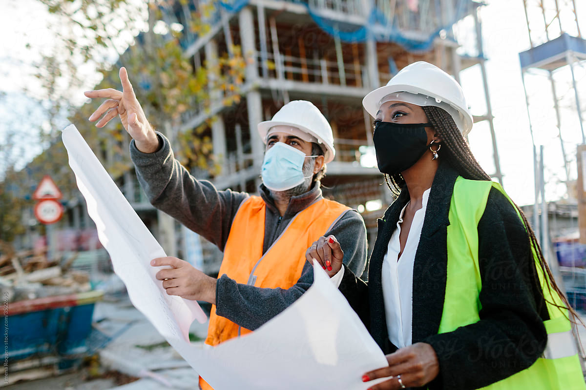 Construction worker reporting to woman engineer while holding some blueprints in front of the construction.