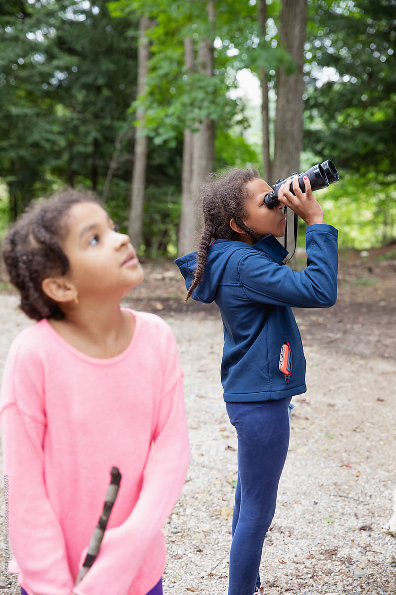 Child looking through a pair of binoculars as her sister stands nearby