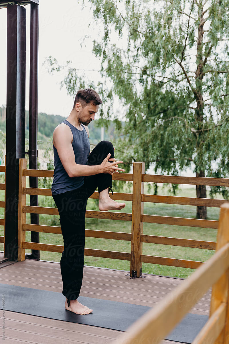 Yoga man practice alone outdoor on a wooden porch and makes asana.