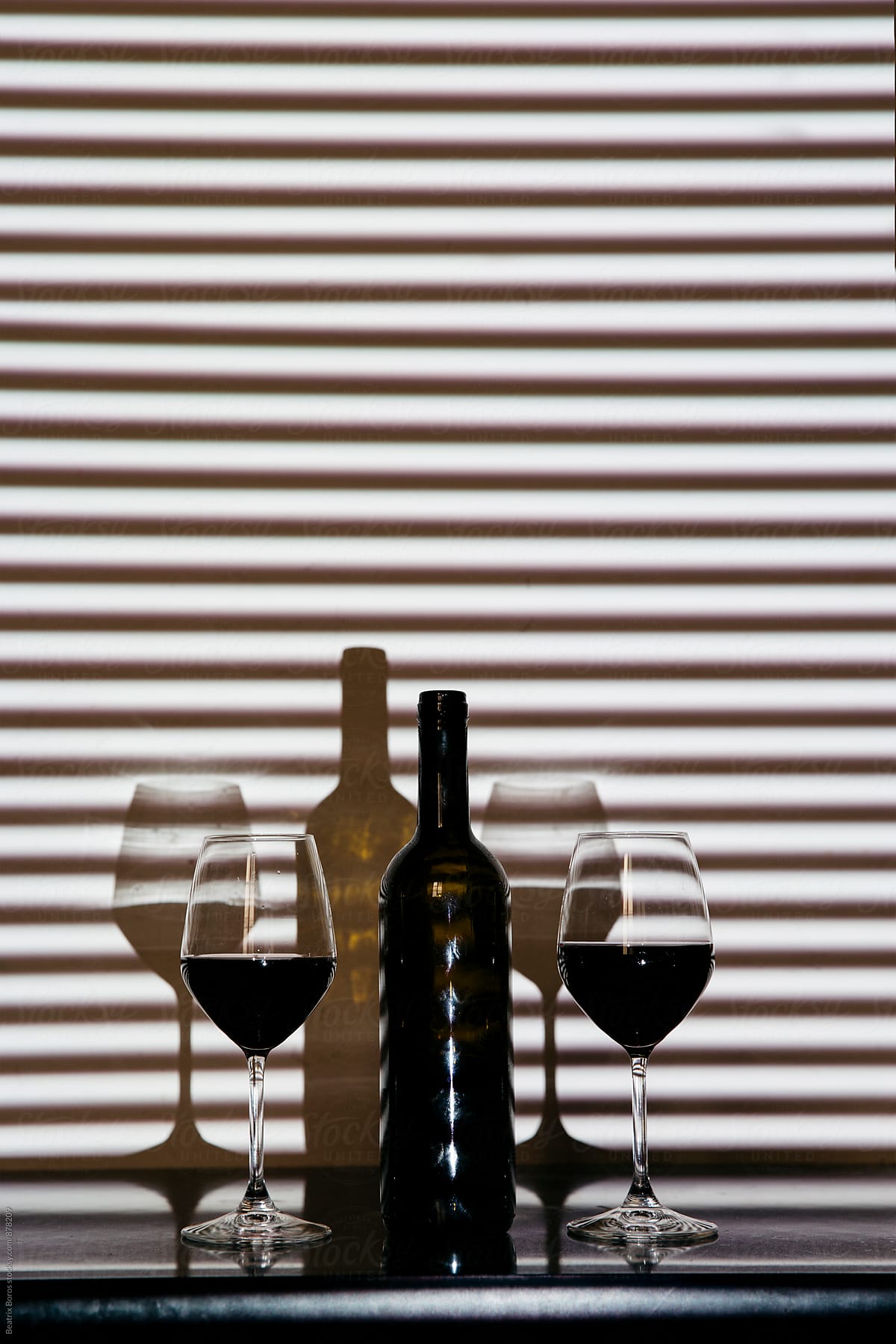 Bottle of wine with two glasses in striped shadow