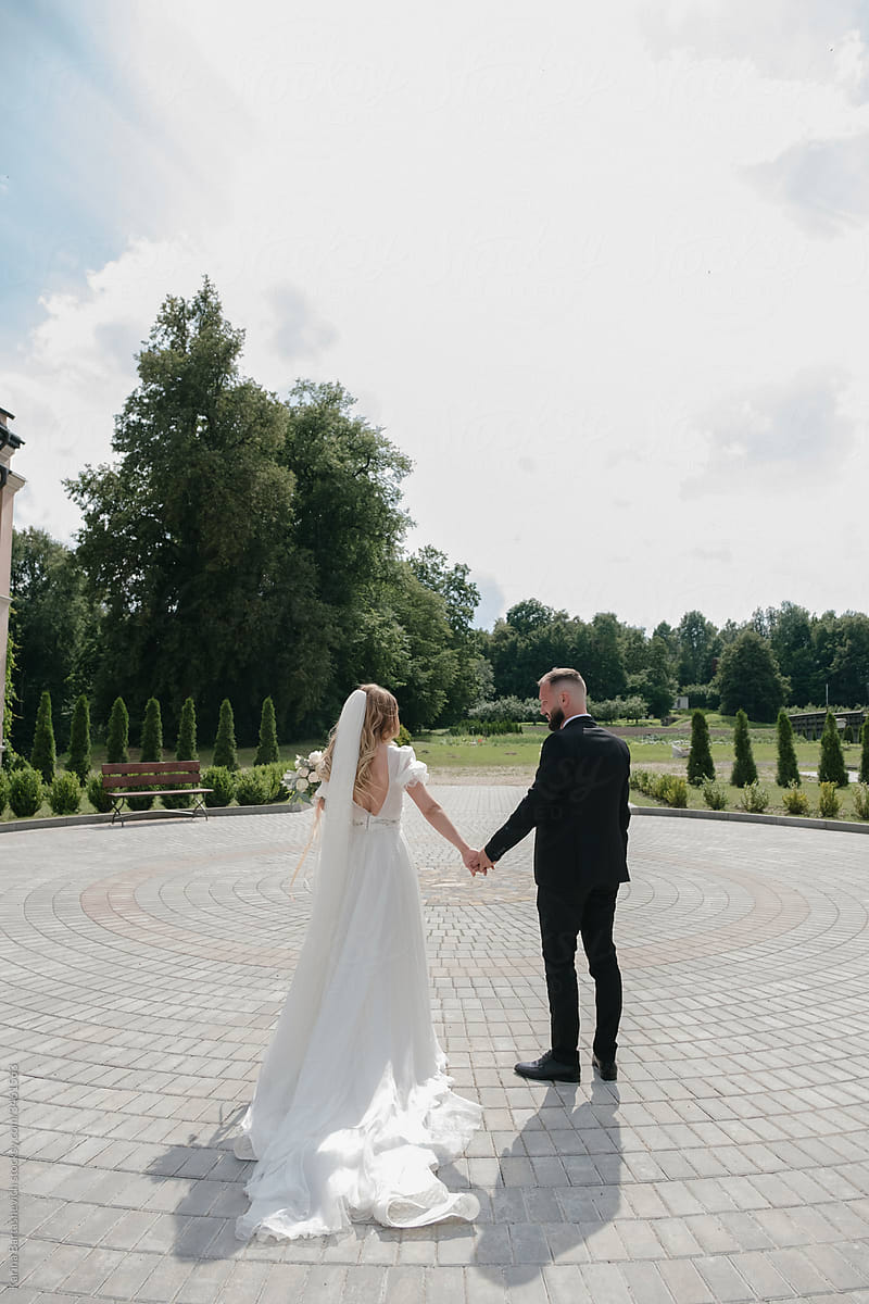 the groom in a black suit and the bride in a white dress hold hands
