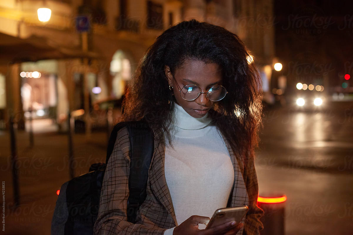 black woman using internet on smartphone at night in the city