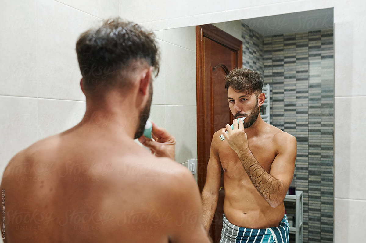 Man brushing his teeth in a bathroom mirror