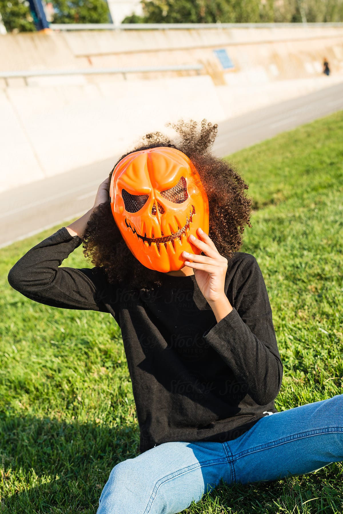 Girl wearing Halloween mask on green grass.