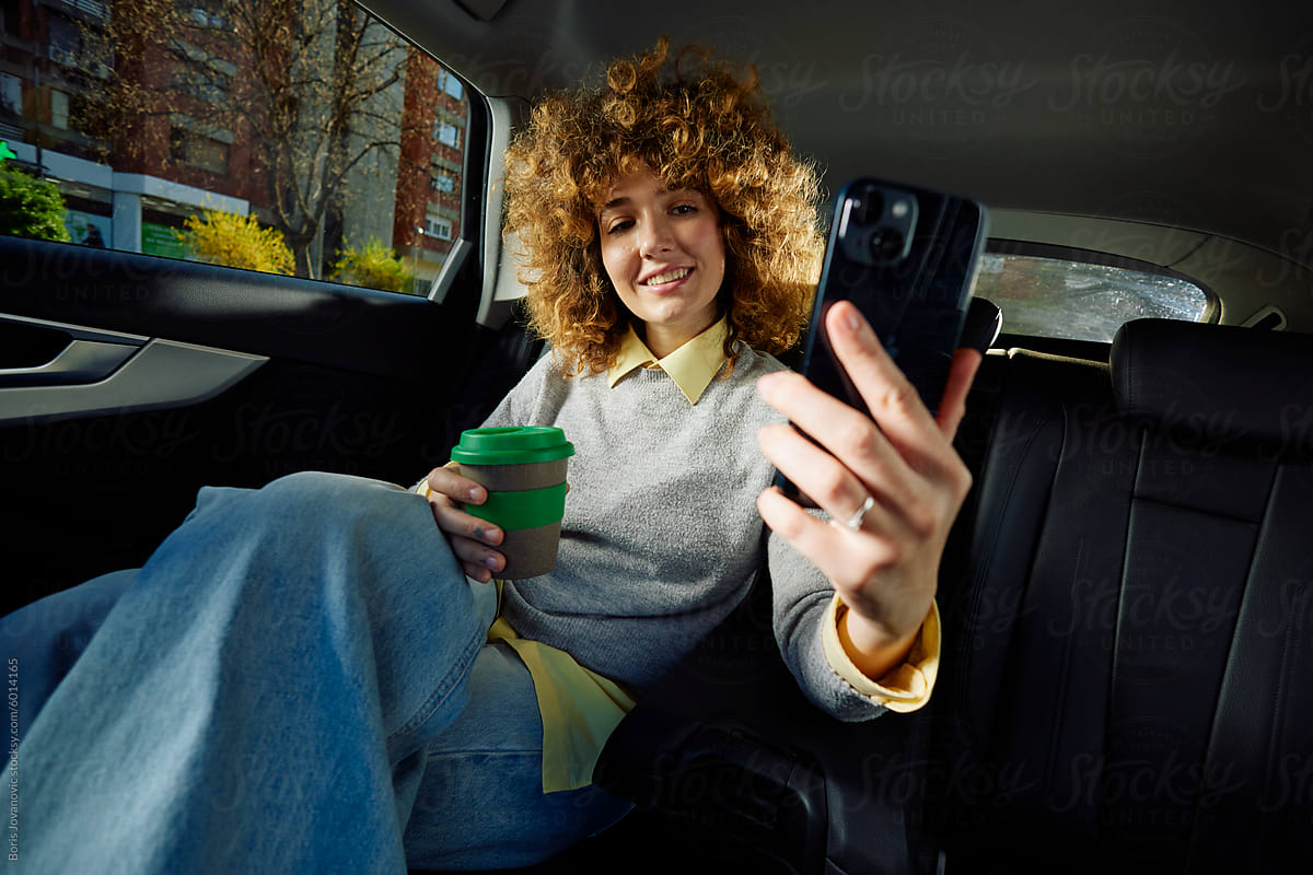 Curly businesswoman taking selfie in a car