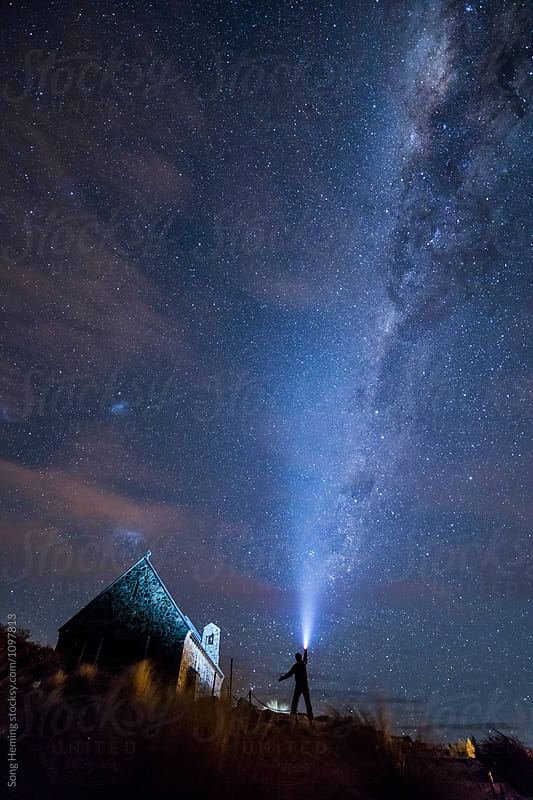 A male adventurer with strong headlamp beside Church of the Good Shepherd under the Galaxy