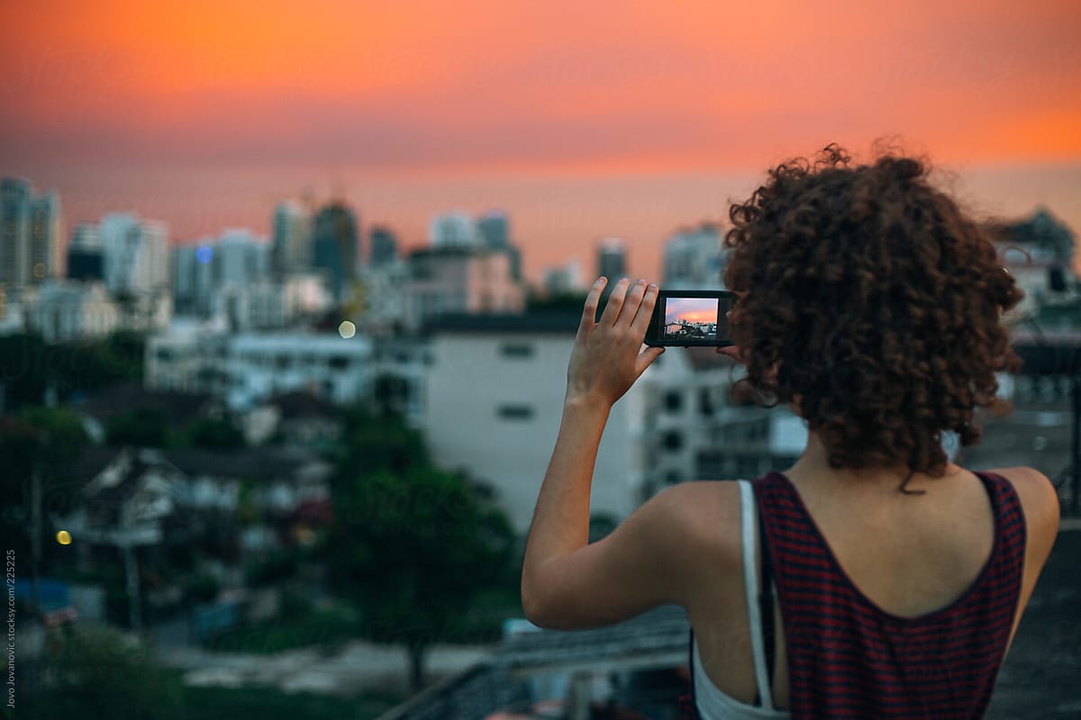 Woman taking photo of beautiful orange sky in the city