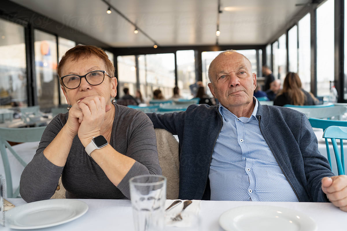Senior Pair Awaiting Meal, Lost In Thought, In A Seaside Restaurant.