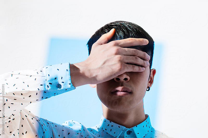 Portrait of an asian man covering his eyes through blue glass.