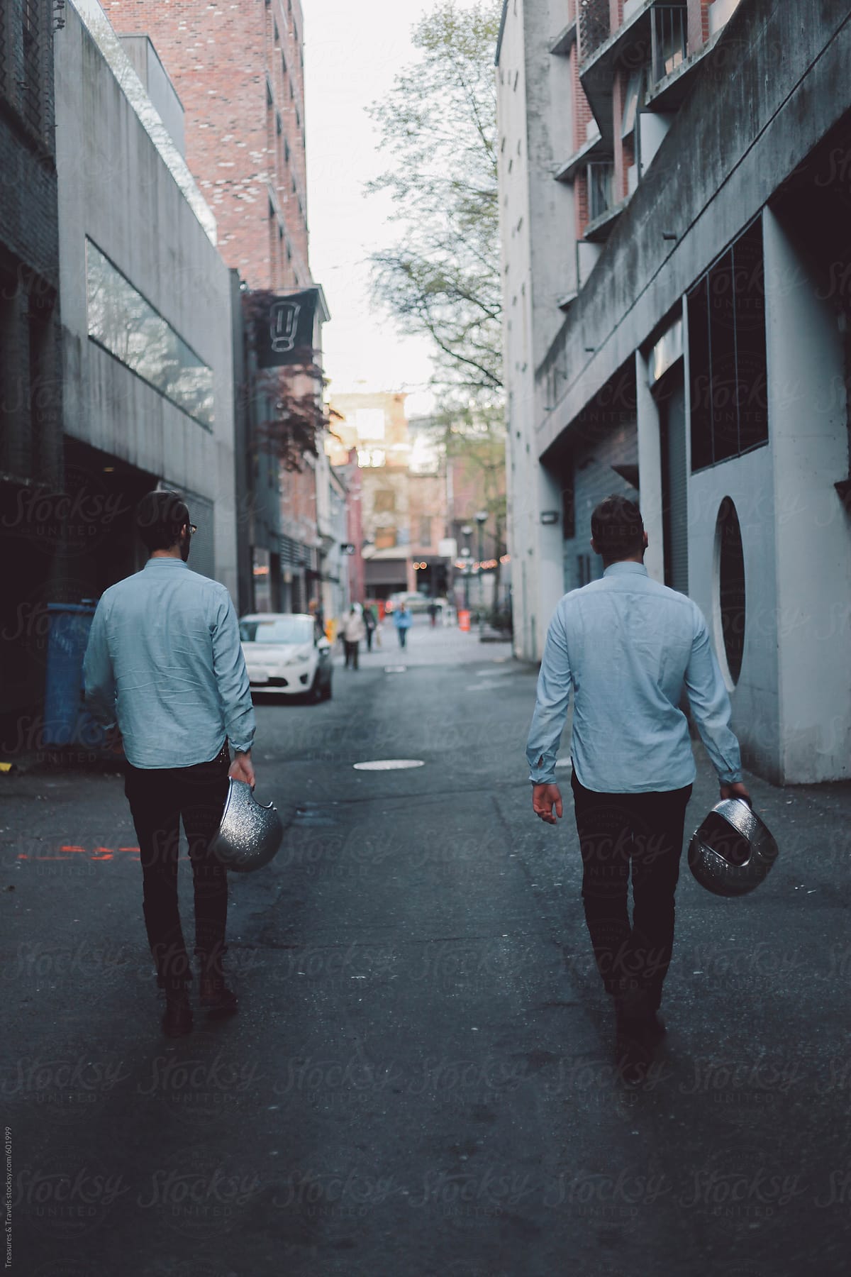 Two young men walking down alleyway holding motorcycle helmets