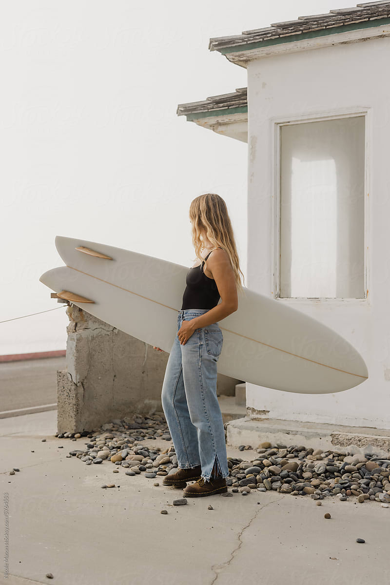 young woman posing with surf board against old white building