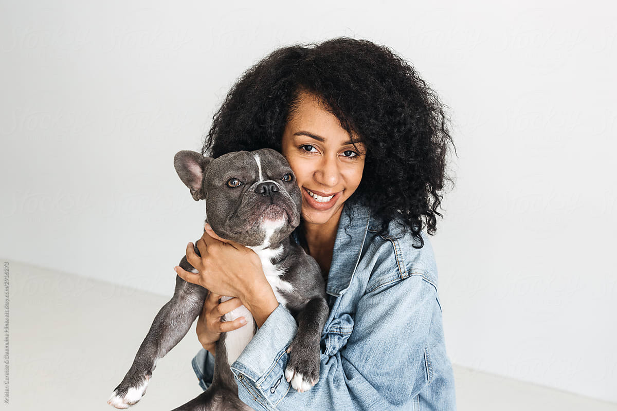 A studio portrait of an African American woman with beautiful curly hair holding a french bulldog.