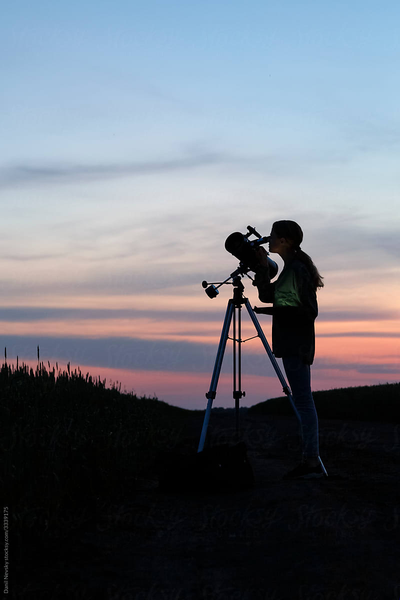 Unrecognizable woman looking at sunset sky through telescope