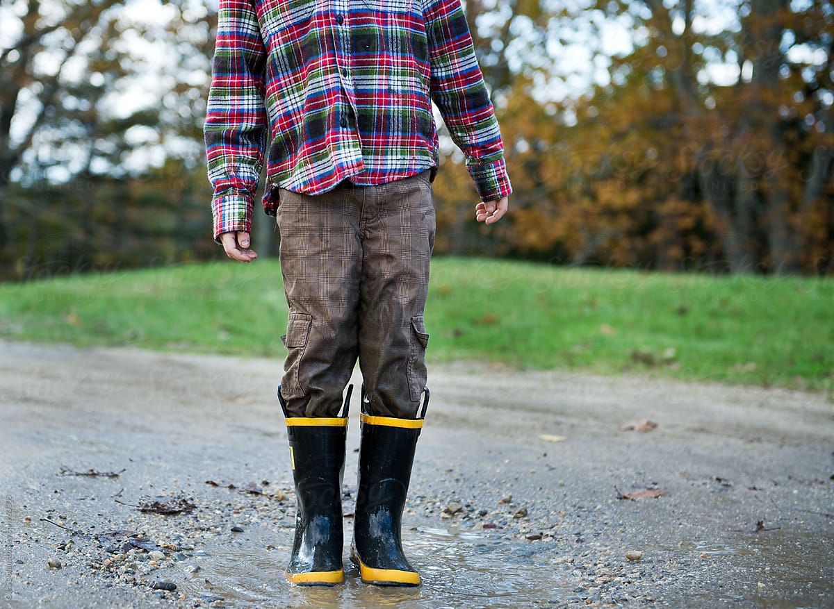 Boy wearing rubber boots stands in a mud puddle