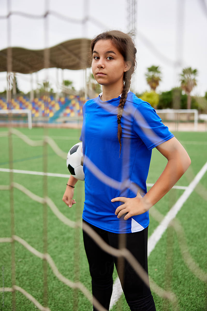 Teen brunette girl with ball standing near goal on field