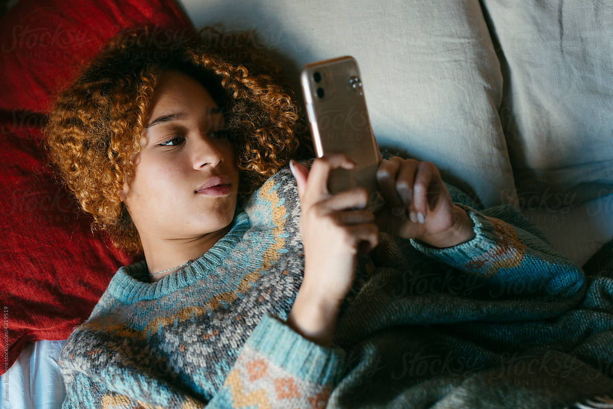 Teenage girl lying on bed checking her smartphone