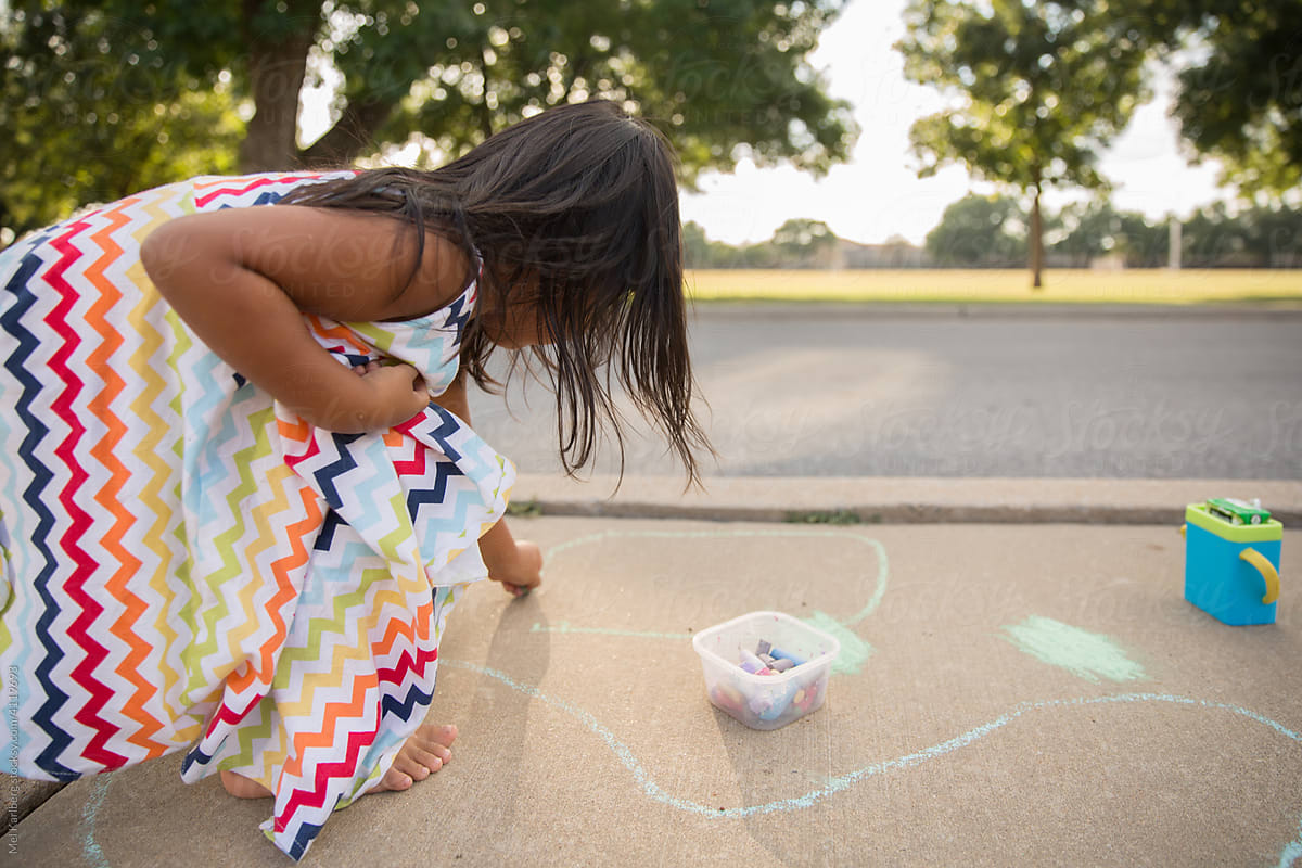 Young girl playing with chalk on neighborhood sidewalk