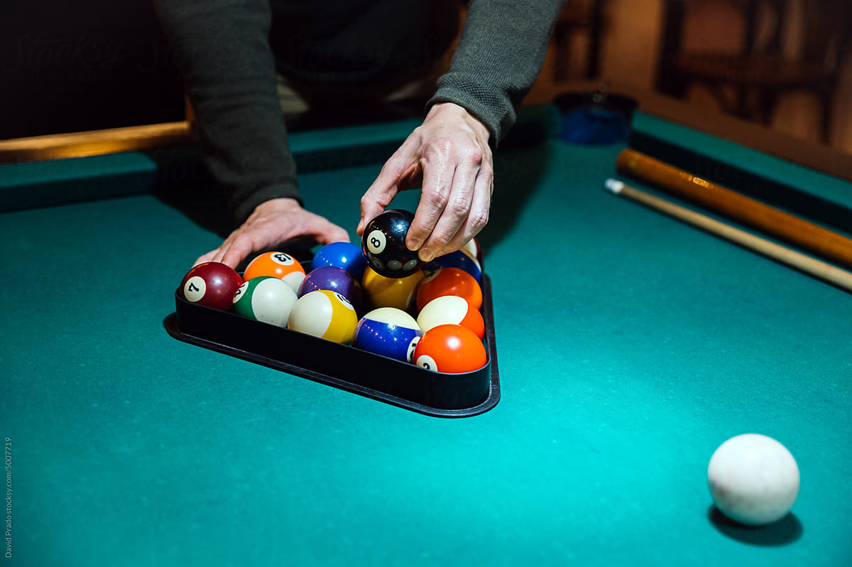 Crop man arranging balls in rack on billiard table