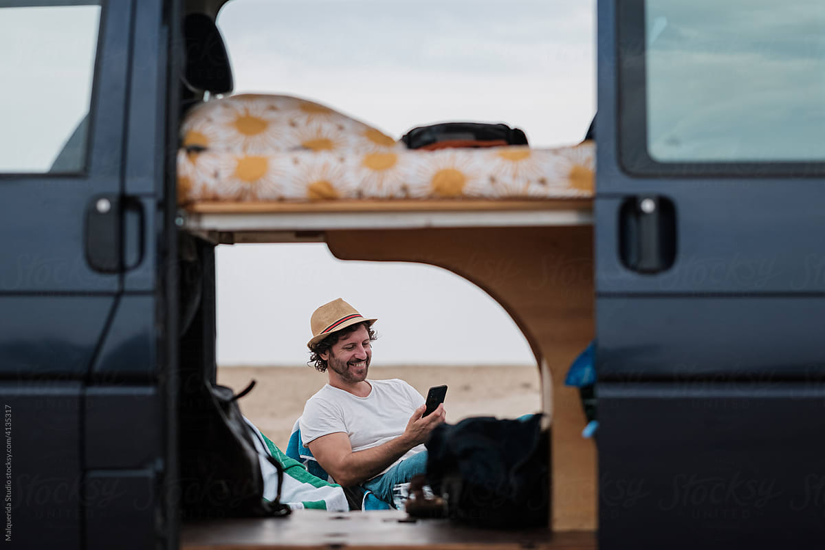 Man looking phone while camping on beach with caravan