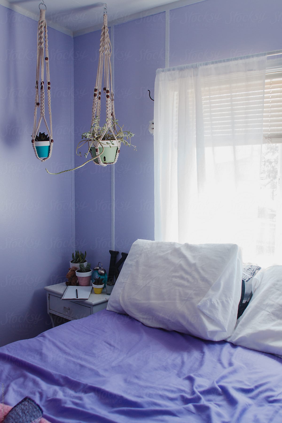 colorful pots hang in macrame next to empty bed w