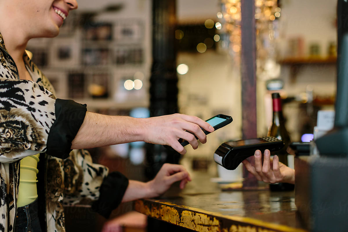 Detail shot of hand holding a smart phone doing a wireless payment at a restaurant