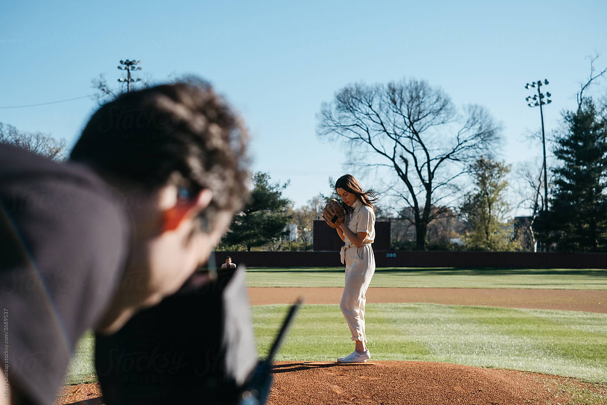 Cinematographer filming a female pitcher on a baseball field
