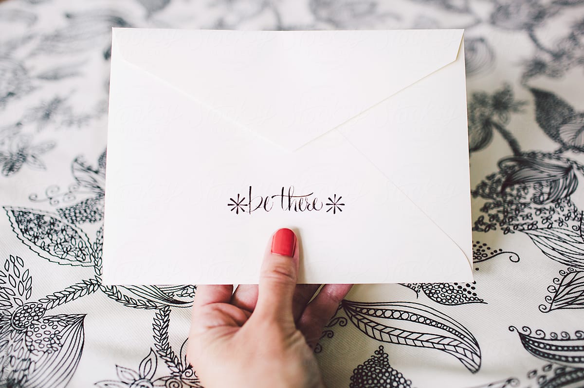 hand holding an invitation envelope with hand lettering that reads \