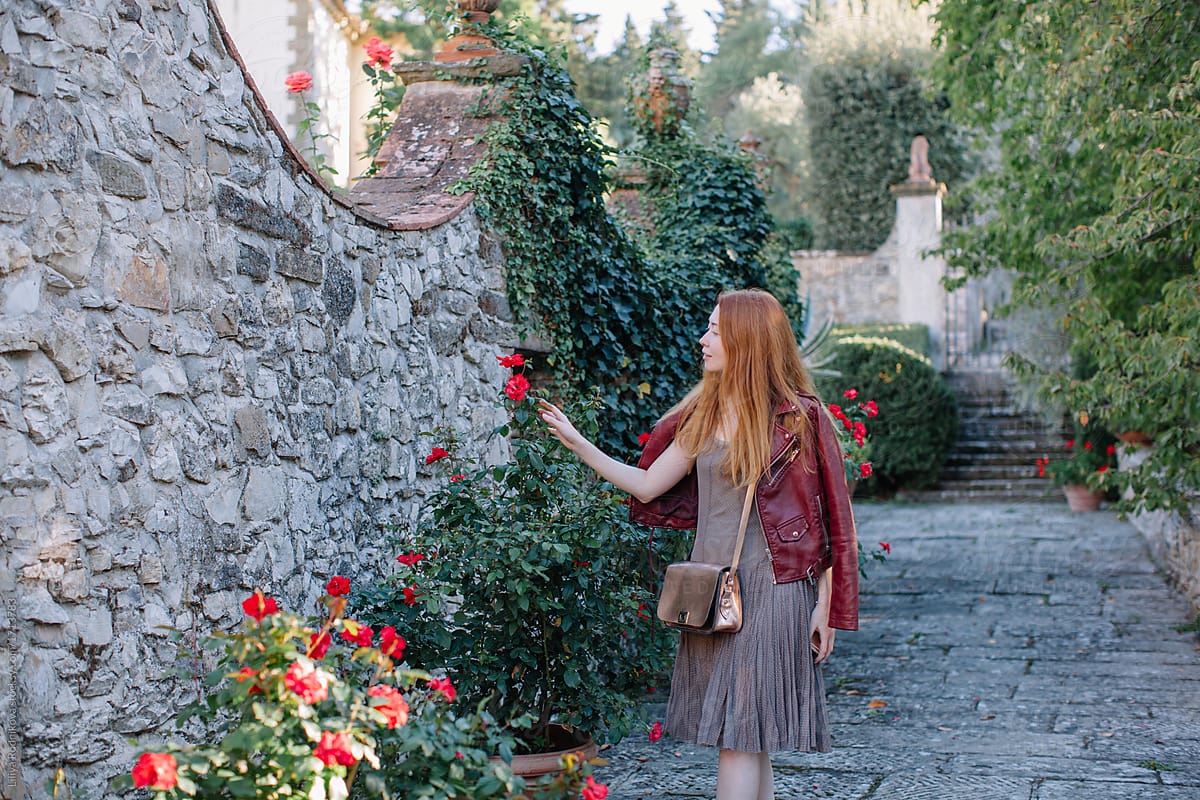 Young redhead woman walking by beautiful garden