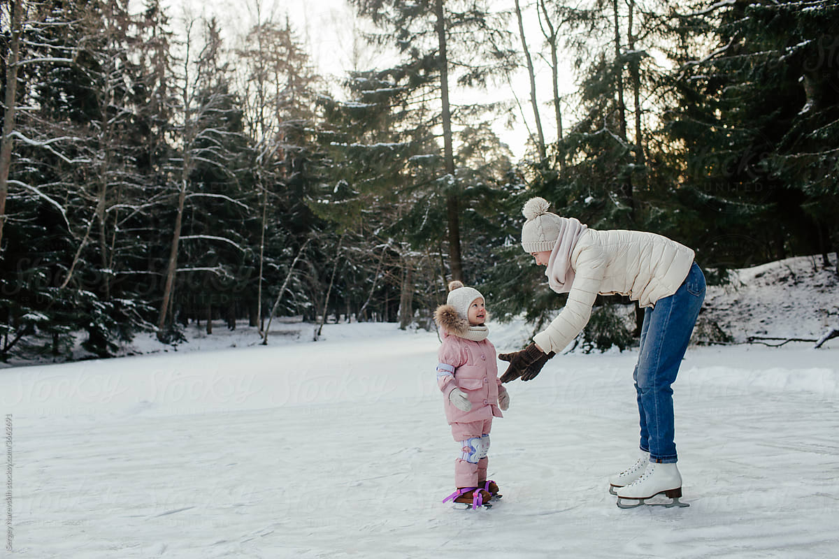 Mother giving help to child learning skating on ice