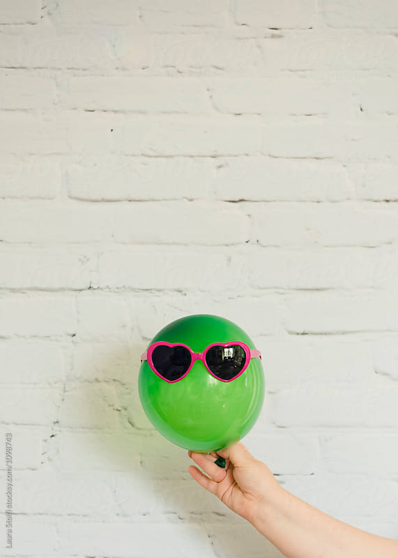 Hand holds a green balloon wearing pink sunglasses