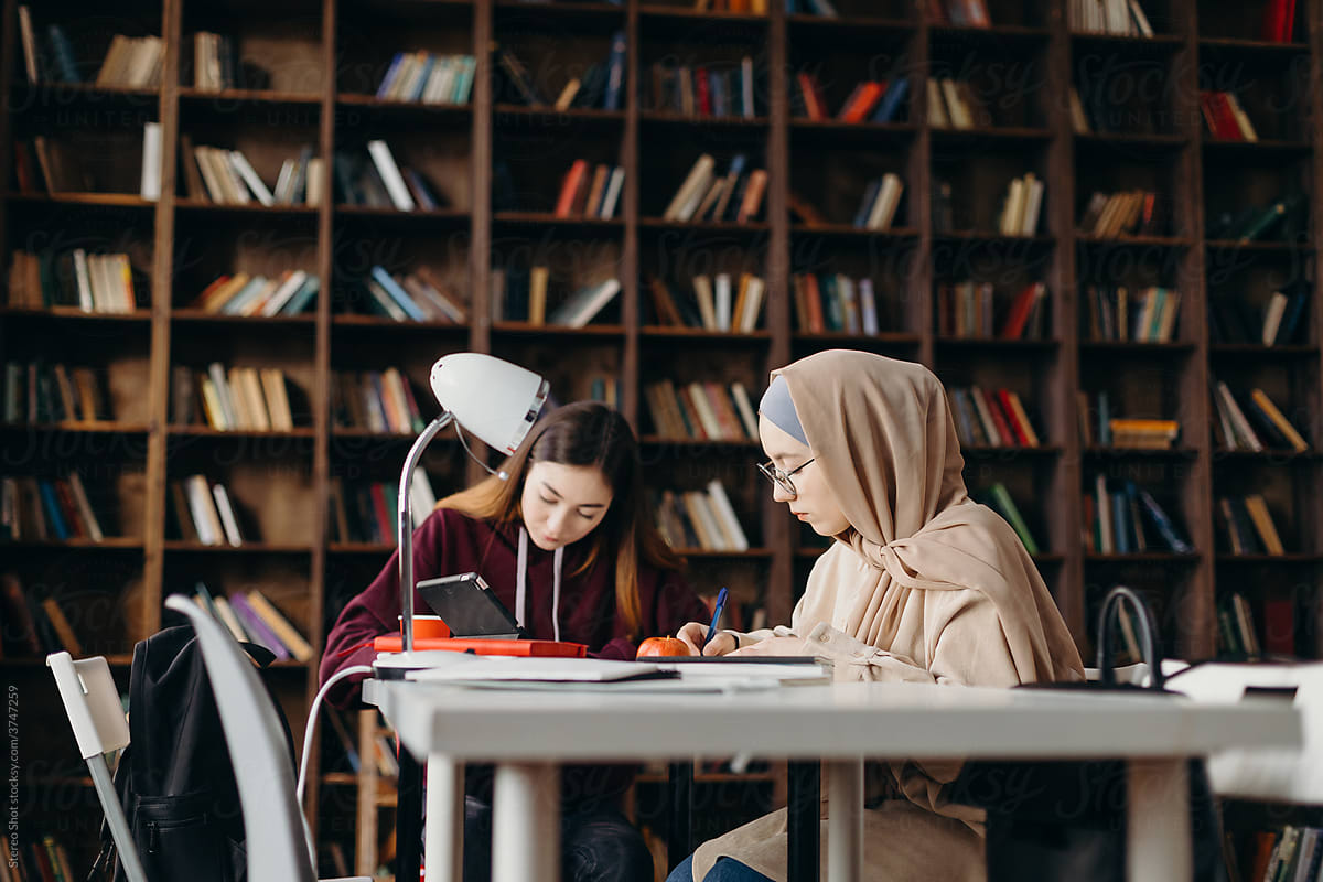 Focused female students fulfilling textbooks in library