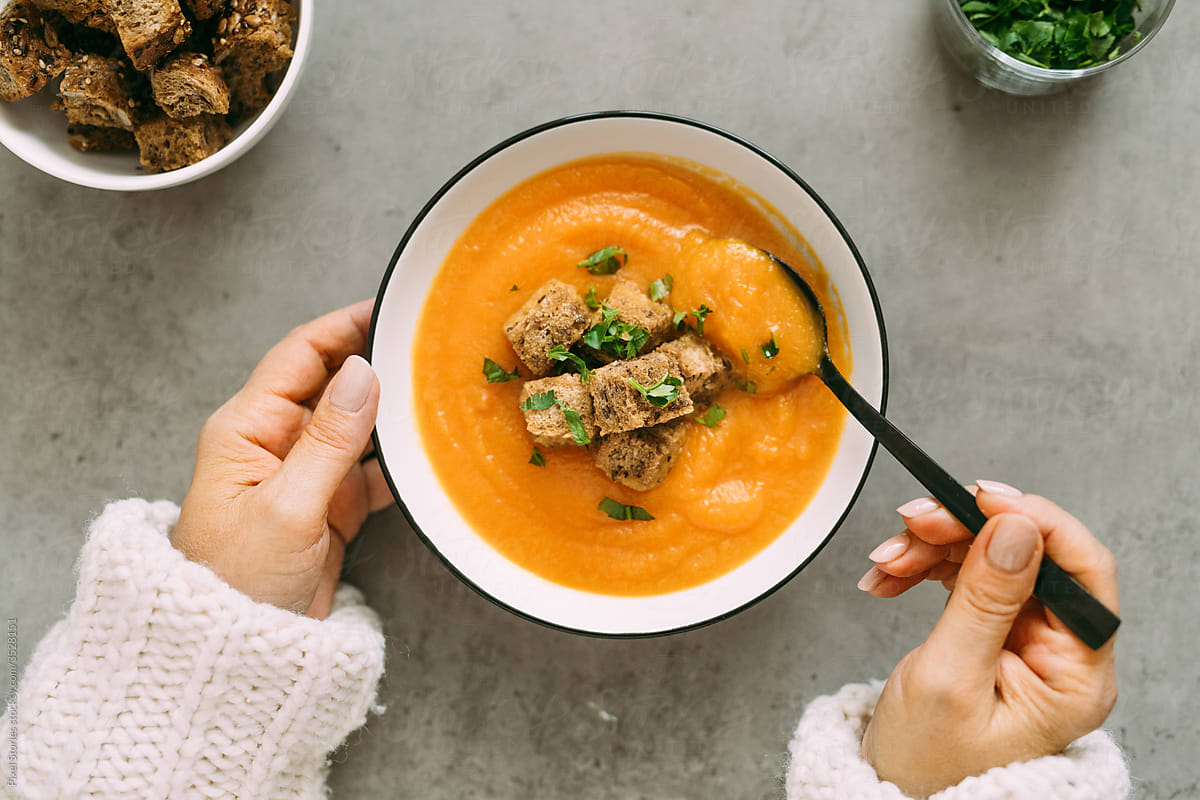Person eats Carrot sweet potato soup with homemade croutons